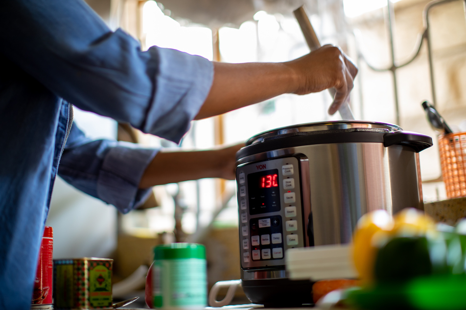 A hand stirring food inside of an electric pressure cooker