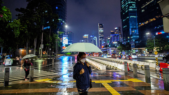 People in the street holding umbrellas and wearing face masks at night