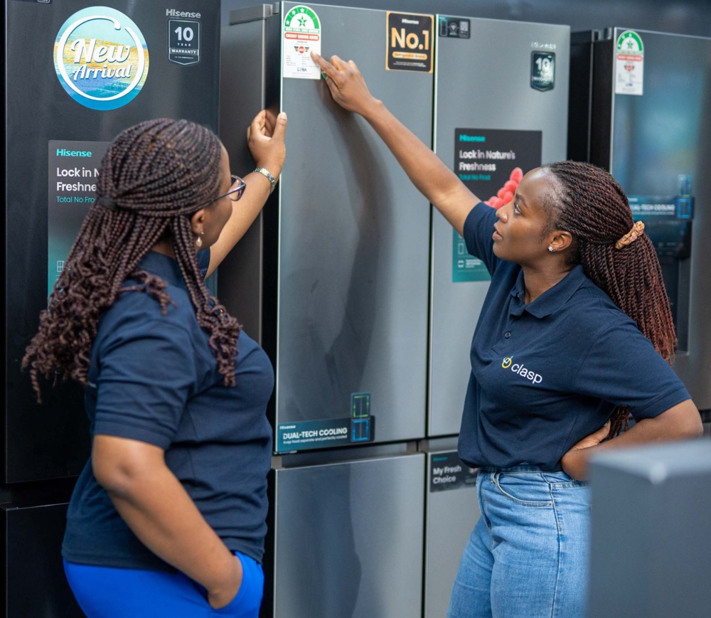 Two women wearing matching CLASP shirts look at an energy efficiency label on a refrigerator in an appliance store.