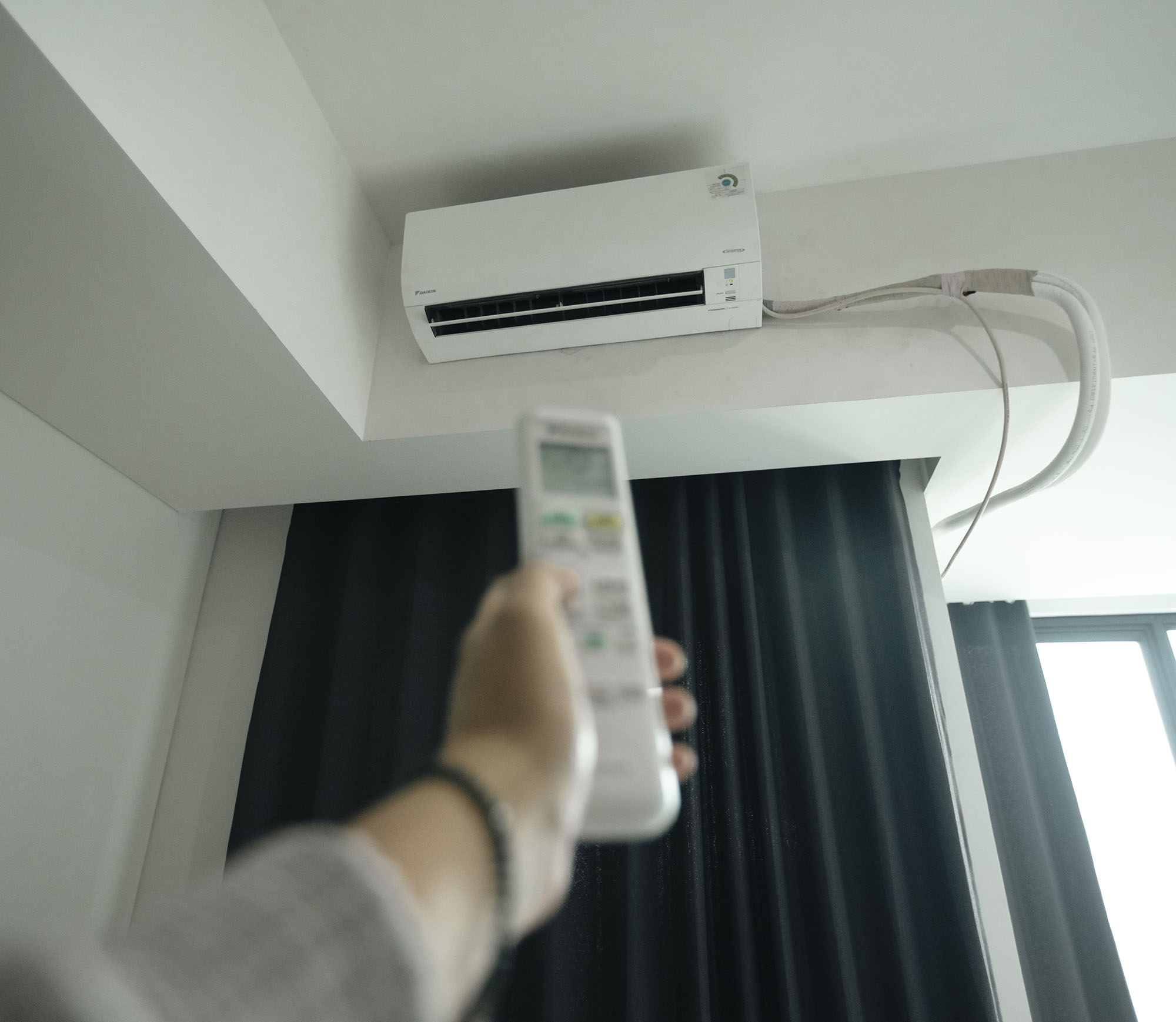 A hand holding a remote control points to a split air conditioning unit.