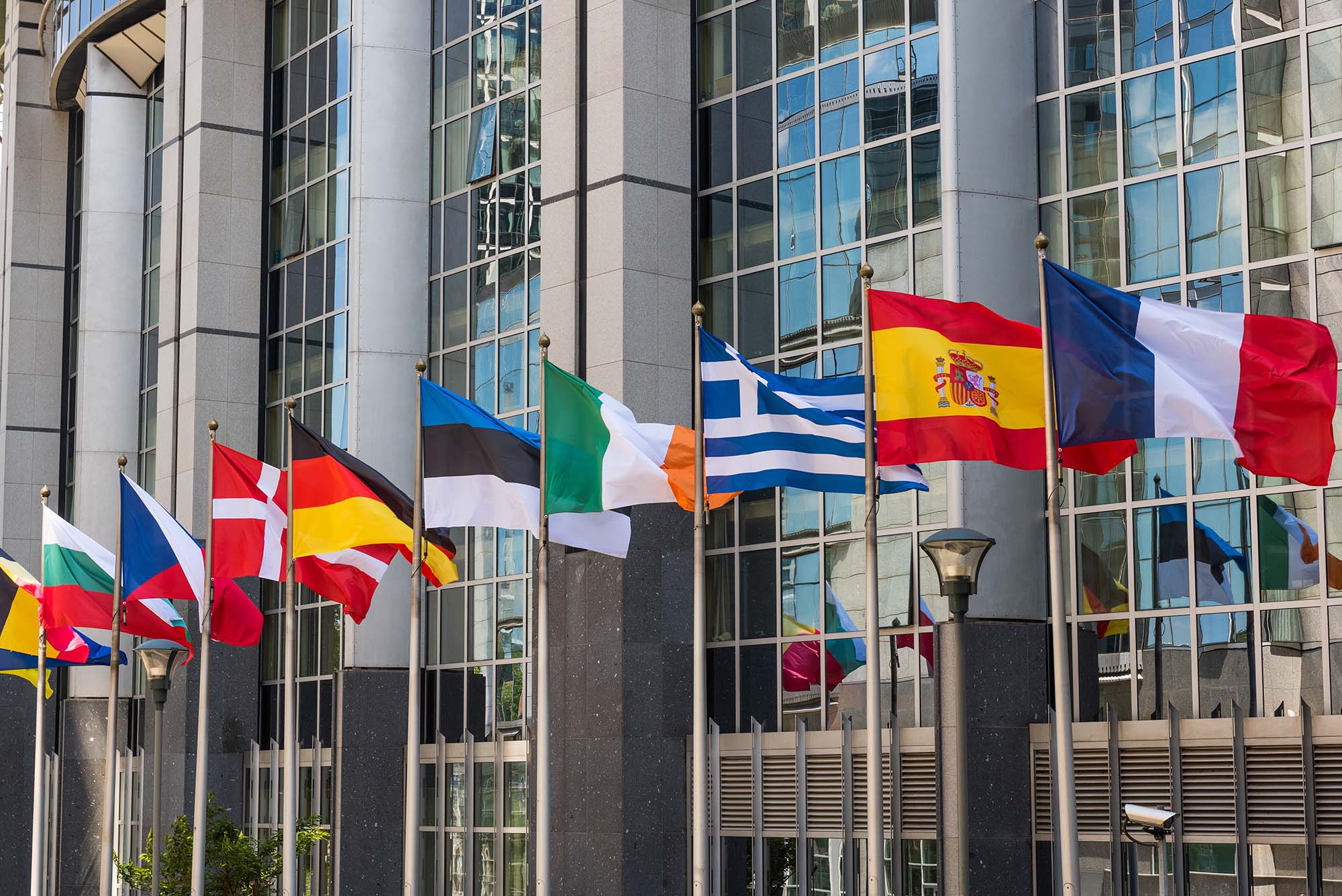 Flags of different European nations wave in front of a glass building