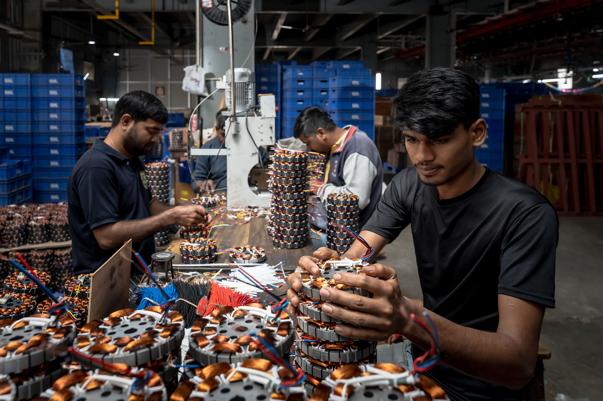 Four men work at a table covered with identical machine parts in a factory.